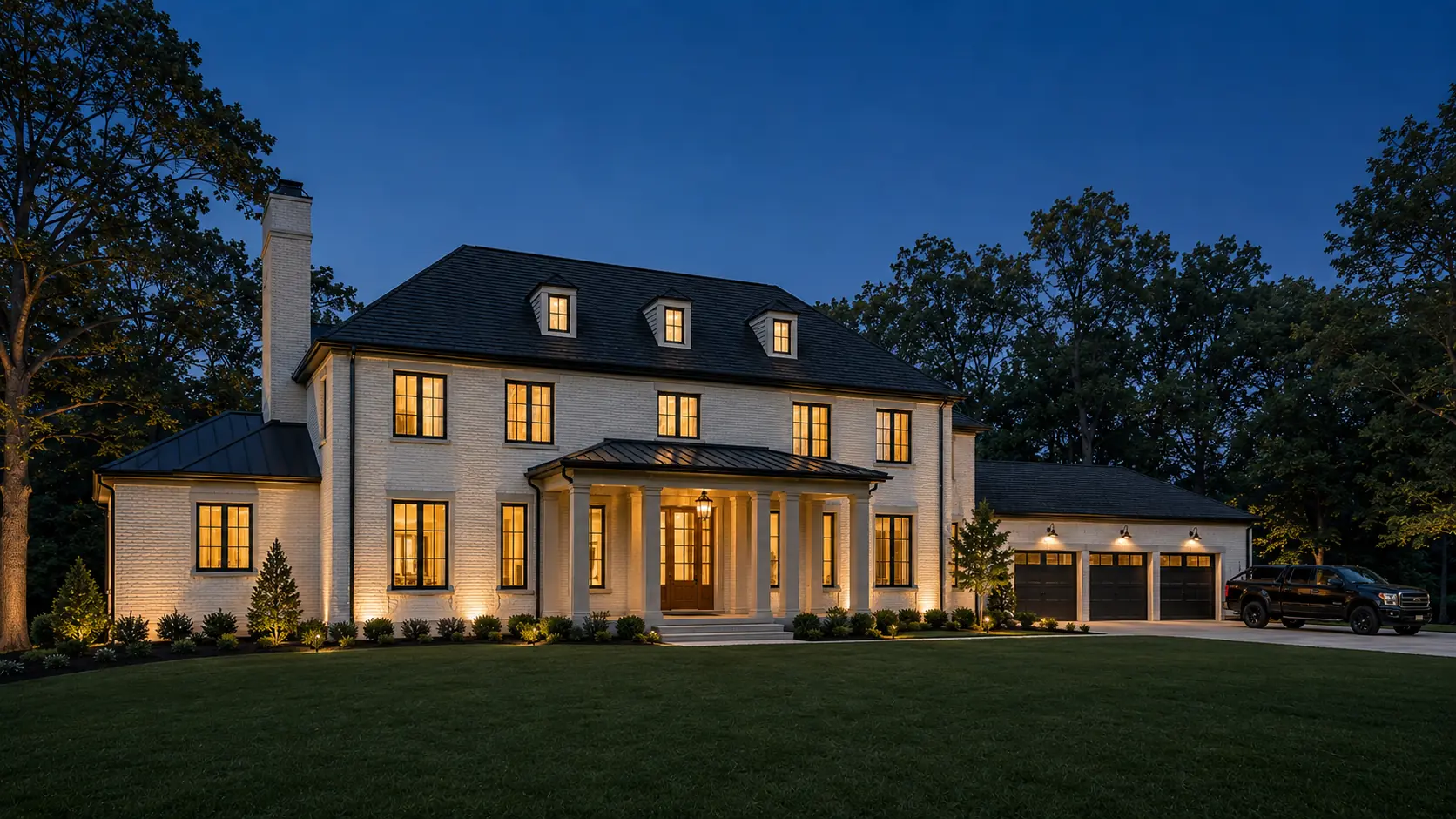 Cinematic blue-hour view of the completed residence with warm interior light glowing through black-framed windows.