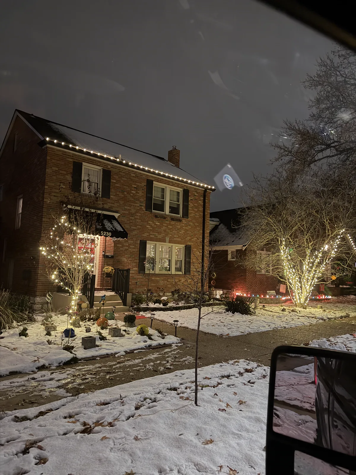 Warm-white roofline lights and lit trees on a brick two-story St. Louis home in the snow