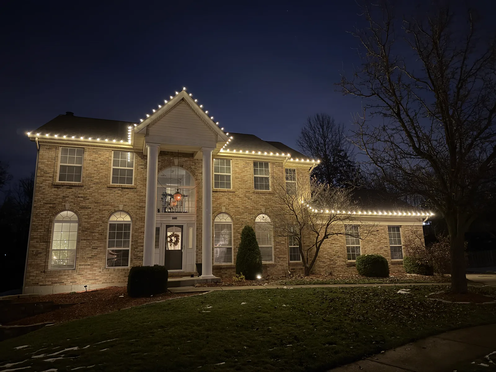 Warm-white C9 roofline lights on a two-story brick colonial with white columns