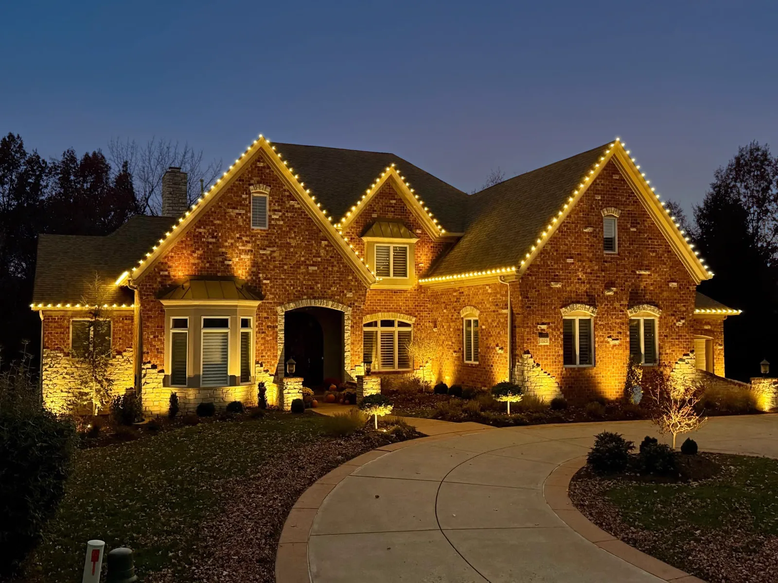 Warm-white roofline lighting and landscape uplighting on a large brick St. Louis-area home