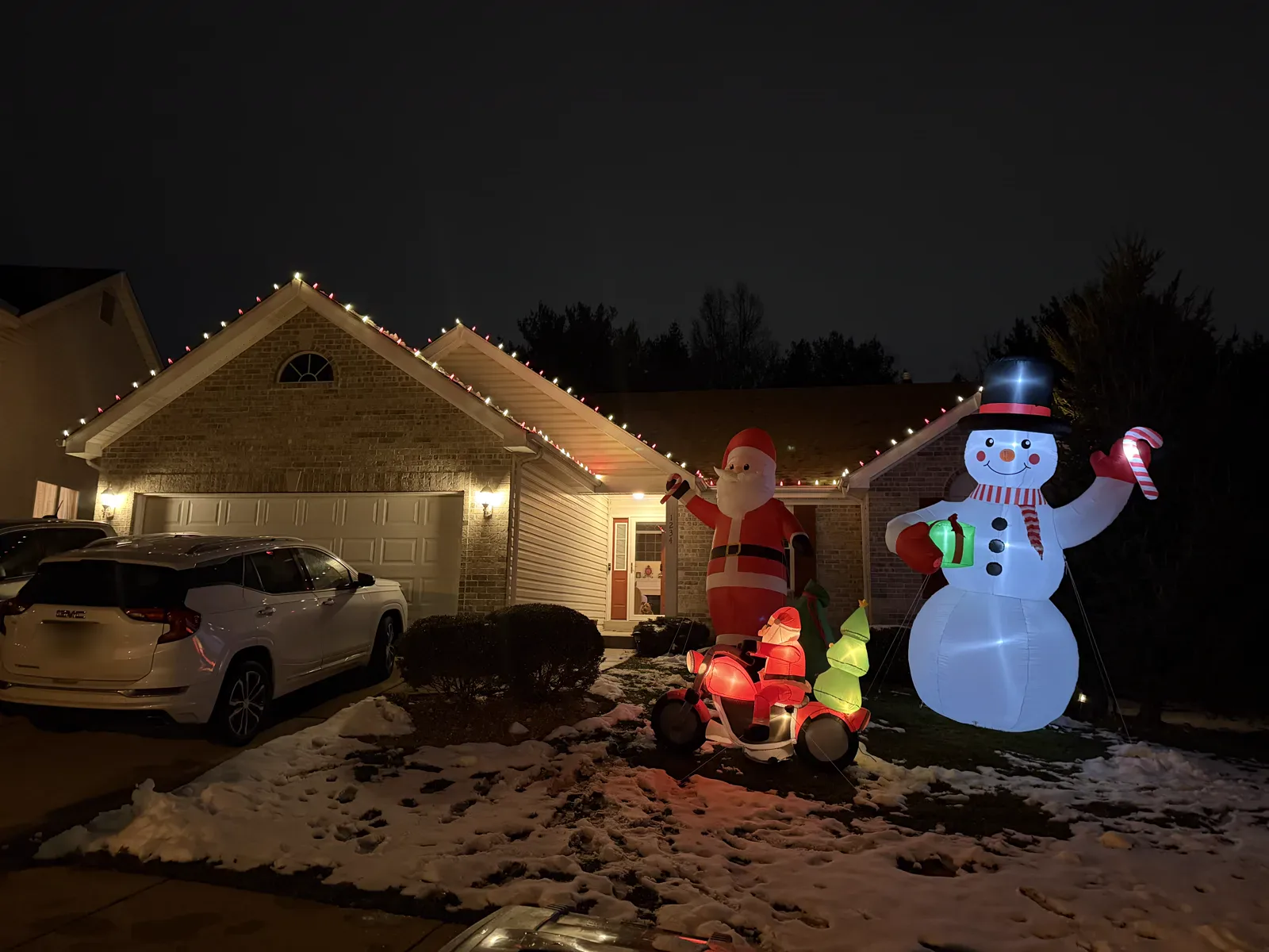 Warm-white and red roofline lights with a full Christmas inflatable display on a St. Louis-area home