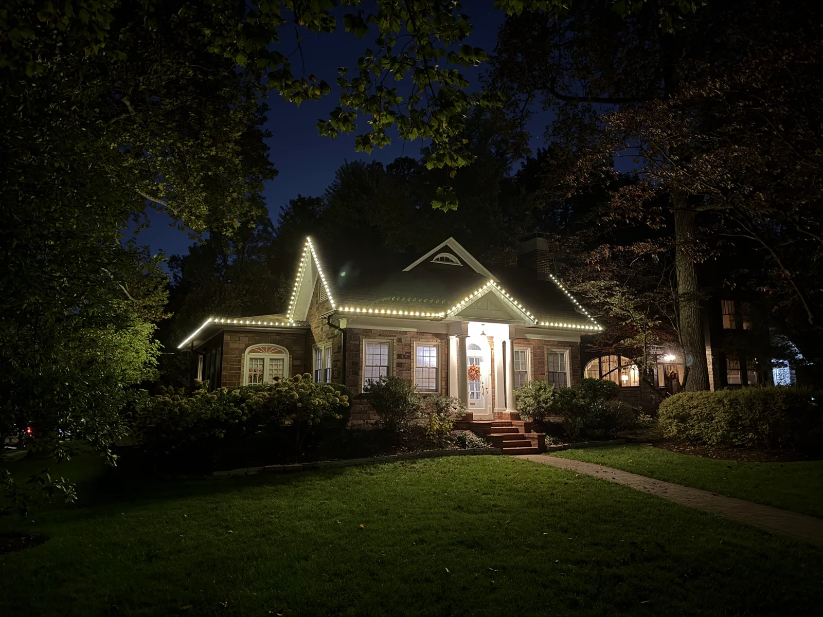 Warm-white roofline lighting on a stone cottage with landscape lighting in the St. Louis area