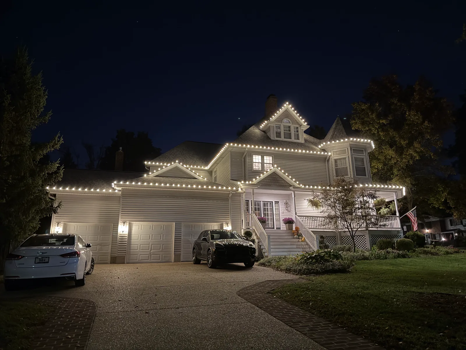 Warm-white roofline lighting outlining a large white Victorian home with a turret