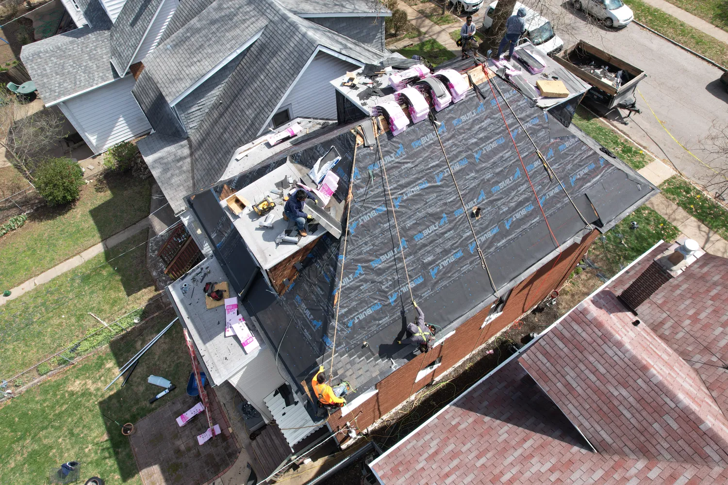 Loxley crew mid-replacement on a two-story brick home with synthetic underlayment installed and shingle bundles staged
