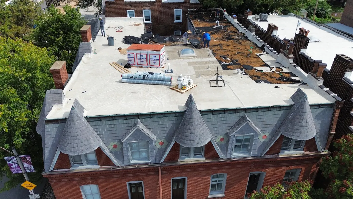 Roofing crew restoring the low-slope roof of a historic St. Louis brick building with a slate mansard