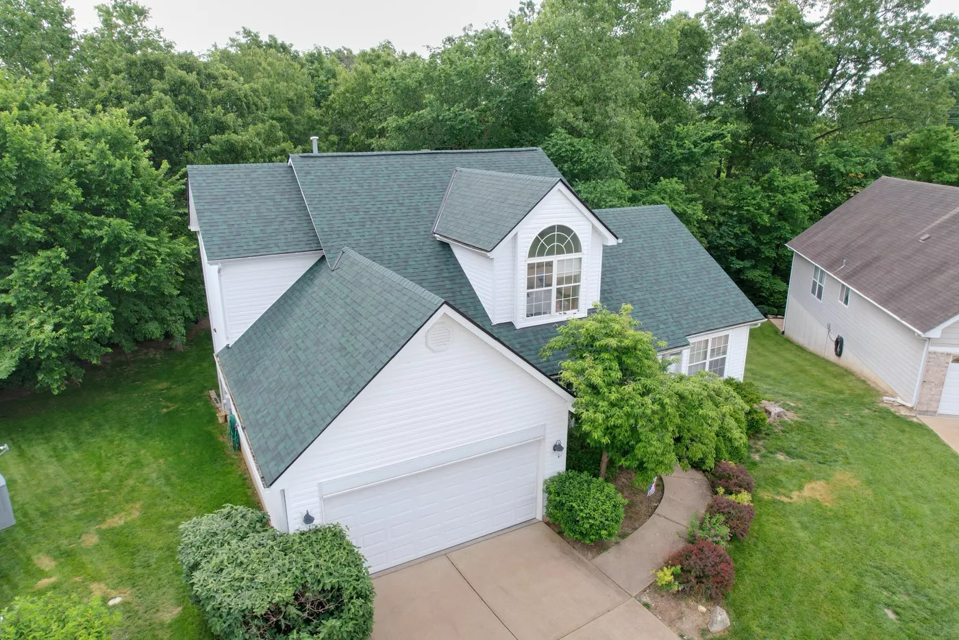Aerial view of a home in a wooded subdivision with a completed green shingle roof