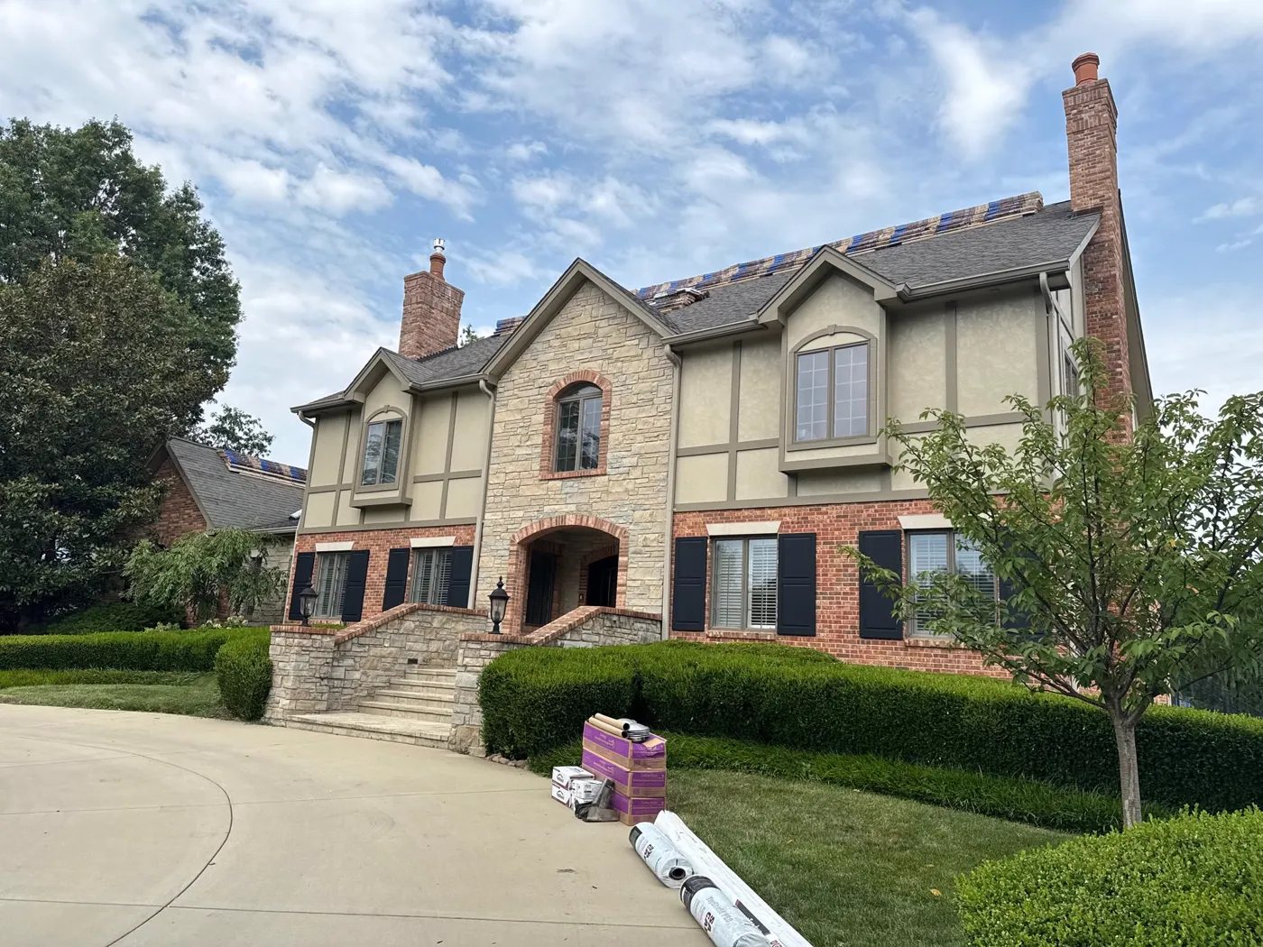 Roof replacement in progress on a large stone-and-stucco Tudor home, new shingles being installed